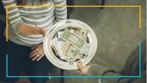 Lady passing an offering plate full of money to a man.